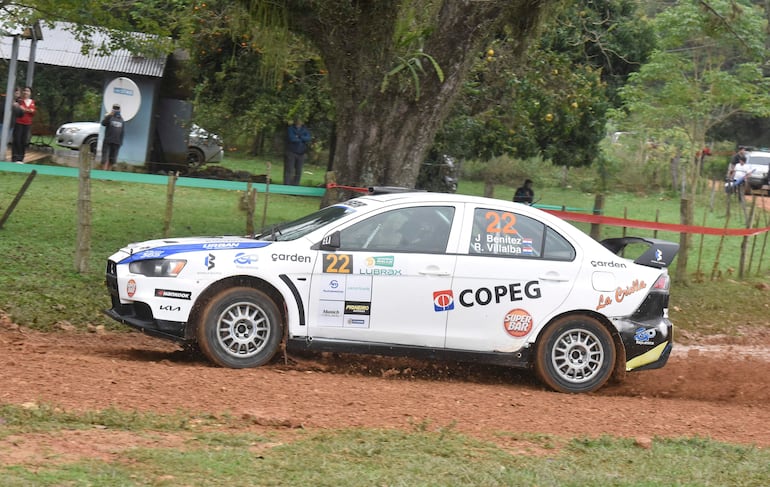 Auto blanco con detalles en azul y negro, número 22, compitiendo en rally con espectadores tomando fotos al fondo.