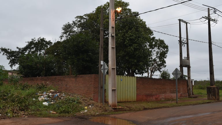 Entorno urbano con dos postes eléctricos, montículo de basura y pared de ladrillo en una calle descuidada.