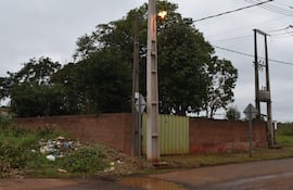Entorno urbano con dos postes eléctricos, montículo de basura y pared de ladrillo en una calle descuidada.