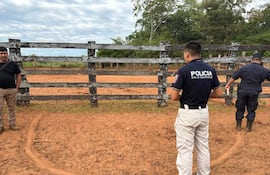 Tres hombres en un terreno con vegetación, dos de espaldas y uno de perfil, uno con camiseta 'POLICIA'.