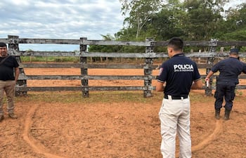 Tres hombres en un terreno con vegetación, dos de espaldas y uno de perfil, uno con camiseta 'POLICIA'.