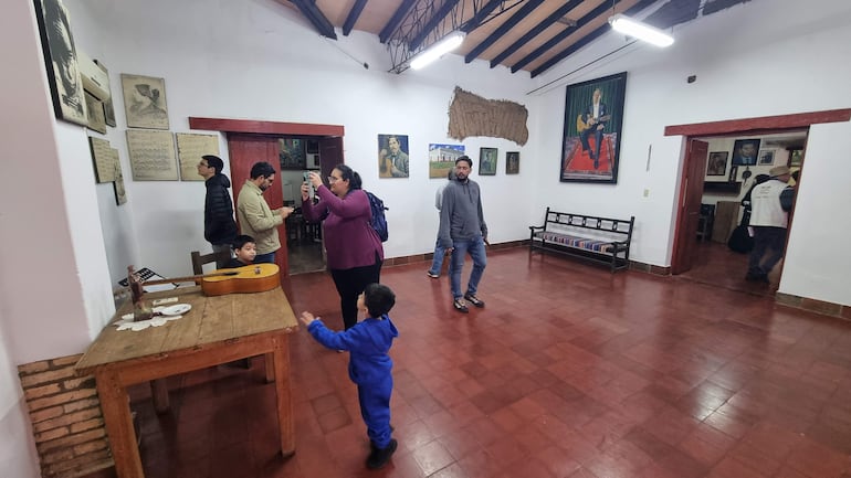Una mujer toma fotos, un niño juega, y hombres observan documentos en el acogedor interior del museo con decoración musical.