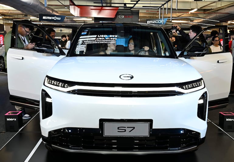 Dos mujeres sentadas en un vehículo eléctrico modelo S7, mientras un hombre toma fotos afuera del automóvil en un evento moderno.