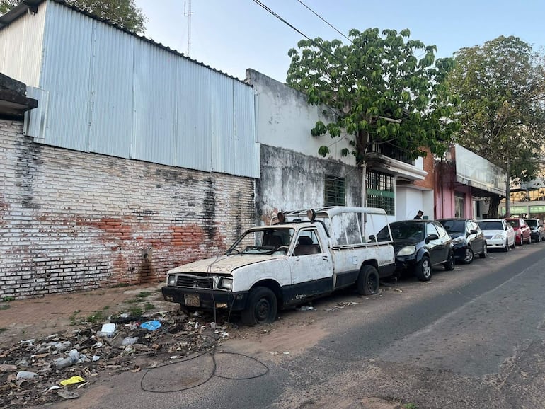 Calle con vehículos en mal estado y basura acumulada, reflejando un ambiente descuidado y urbano desolado.