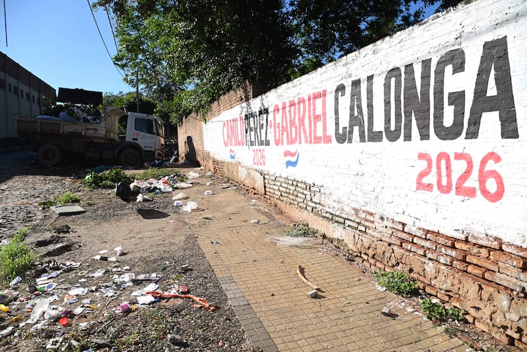 Camión de recolección semi-cargado junto a un muro con el texto 'CAMILO PÉREZ GABRIEL CALONGA 2026' en un entorno descuidado.