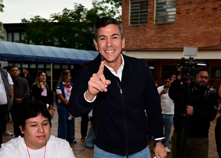 Santiago Peña en chaqueta oscura y camisa blanca, levantando un dedo marcado, mientras César Rossel lo observa.