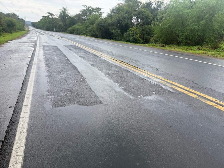 Carretera en mal estado, con surcos y vegetación densa a la derecha, bajo un cielo nublado.