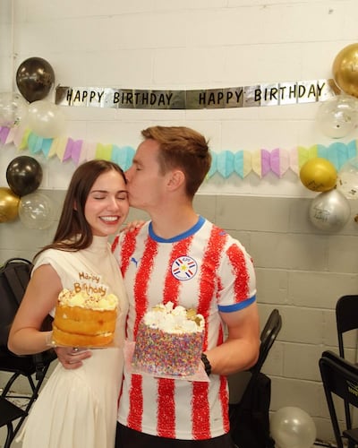 Joshua Duerksen sonríe con camiseta de rayas, mientras Anneke Rahn luce un vestido blanco y sostiene un pastel con velas.
