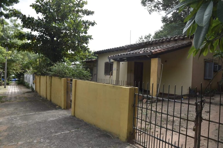 Casa amarilla con techo de tejas, camino de cemento y vegetación frondosa en su alrededor.