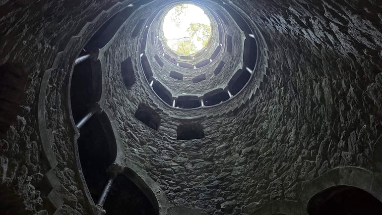 Interior de una estructura arquitectónica antigua con pozo circular iluminado por luz natural, sin personas presentes.