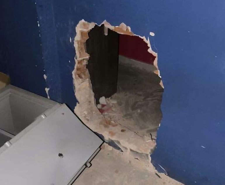 Agujero en la pared de una casa de cambios con un congelador gris abierto a la izquierda, suelo cubierto de polvo.