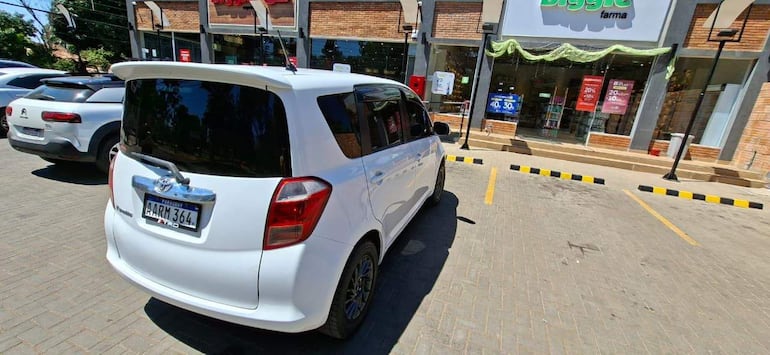 Estacionamiento con vehículos blancos y carteles promocionales visibles de la tienda Biggie, sin personas presentes.