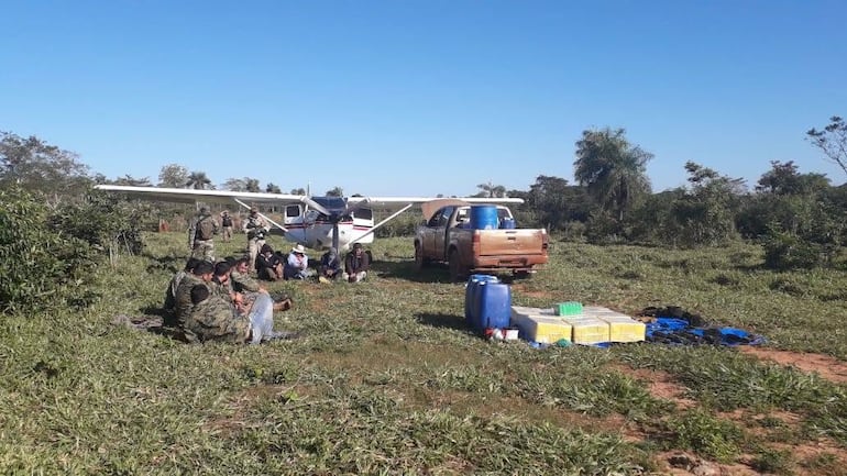 Cerca de la carga de cocaína proveniente de Bolivia están sentados los agentes policiales que, momentos antes intentaron extorsionar a los narcotraficantes (sentados casi debajo de la aeronave con matrícula boliviana).