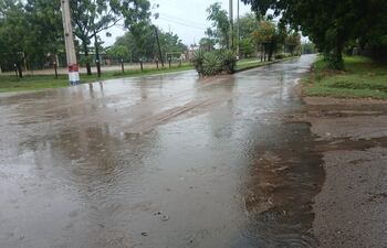 Calle con asfalto mojado y charcos tras lluvia intensa, flanqueada por árboles y postes de electricidad, sin personas visibles.