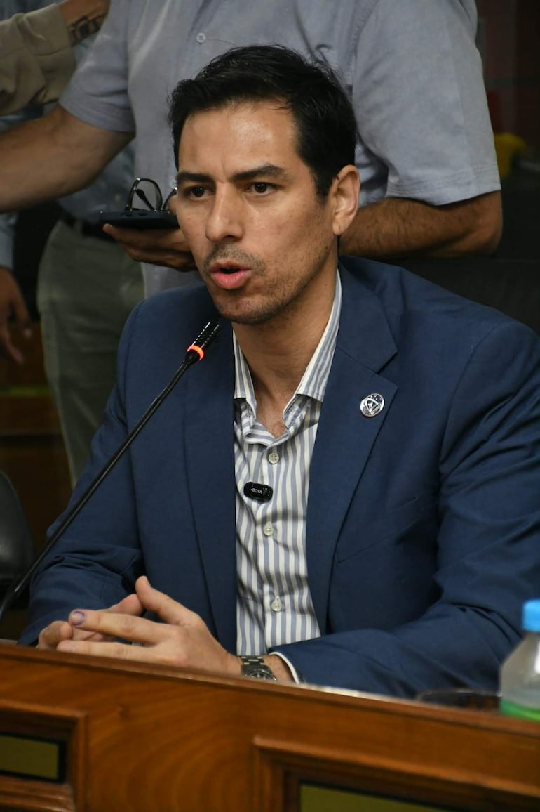 Alvaro Grau en blazer azul oscuro y camisa de rayas, habla al micrófono en un ambiente formal con otros presentes.