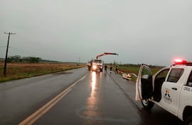 Cinco personas supervisan trabajos en carretera, con camión de Itaipú Binacional y vehículo policial presente en un día lluvioso.