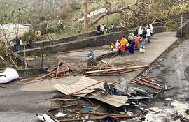 A photo taken on December 15, 2024 shows residents sitting by a road among piles of debris of metal sheets and wood after the cyclone Chido hit France's Indian Ocean territory of Mayotte. At least 14 people were killed in Mayotte when a fierce cyclone battered the French Indian Ocean territ)ory, authorities said on December 15, 2024, with officials warning it will take days to know the full toll. (Photo by KWEZI / AFP