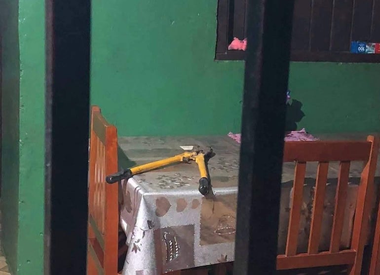 Ambiente interior con mesa y sillas desordenadas, objeto amarillo sobre mantel con diseño de hojas.