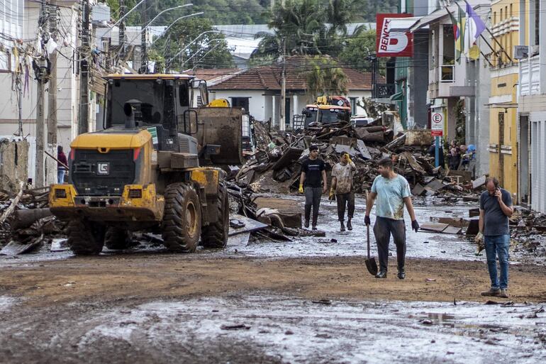 Fotografía cedida por el Gobierno del estado de Rio Grande do Sul que muestra a unas personas junto a un vehículo de maquinaria pesada mientras despejan una calle inundada por las torrenciales lluvias, en Muçum, estado de Rio Grande do Sul (Brasil).