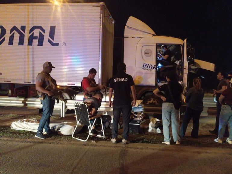 Hombres armados revisan un camión con el logo 'DINAF', en una noche de operativo, mientras otros observan atentos.