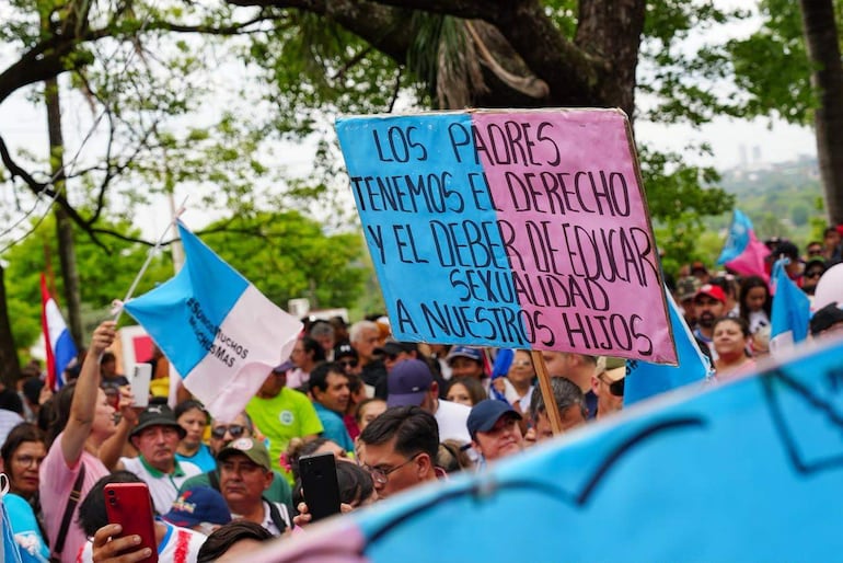 Manifestantes sostienen carteles en protesta, con banderas azul y blanca ondeando en un ambiente urbano.