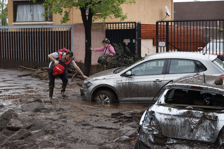 Personas intentan caminar en medio del lodo tras el paso de un aluvión en la comuna de Las Condes.
