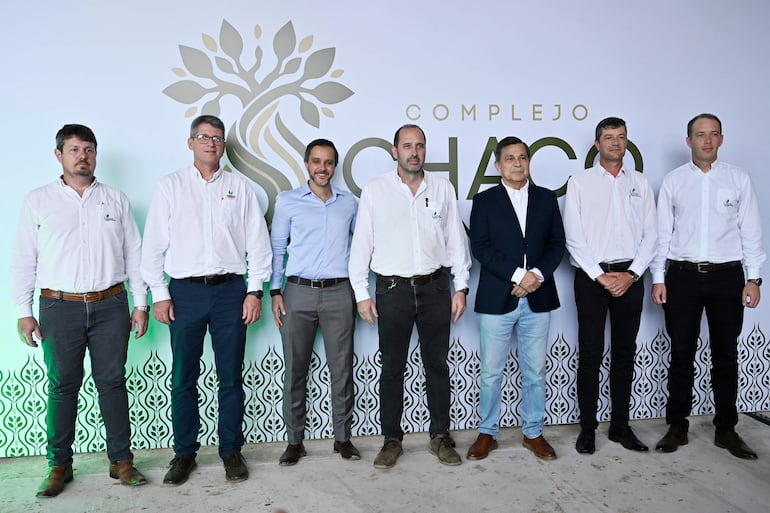Seis hombres de pie con camisas blancas, alineados frente al logo del Complejo Chaco, mostrando expresiones tranquilas y felices.