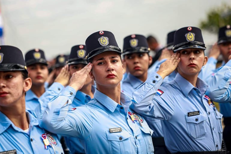 Mujeres policías en uniforme azul claro y gorras negras realizan saludo militar, alineadas y concentradas en un punto fuera de la imagen.