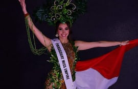 Mujer sonriente con vestido decorado y bandera de Paraguay en mano, en un ambiente formal y oscuro.