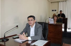 Hombre de cabello corto y canoso en saco gris escucha atentamente. Mujer con cabello largo sostiene documentos. Ambiente formal y sereno.