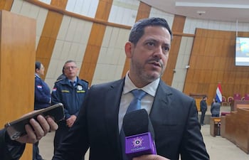 Raúl Latorre en traje oscuro y corbata celeste, hablando ante un micrófono mientras es observado por asistentes en un ambiente formal.