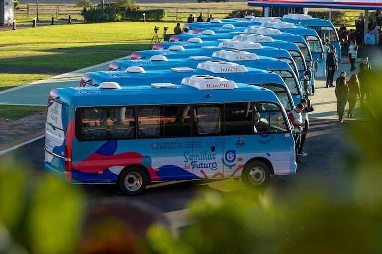 Autobuses azules con el logo 'Semillas del Futuro' alineados, rodeados de personas observando en un parque.