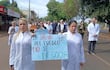 Médicos en batas blancas sosteniendo pancarta con lema sobre la salud, en un ambiente de protesta pacífica en la calle.