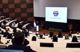 Manuel Ochipintti en traje oscuro, hablando desde un atril, mientras asistentes en trajes formales escuchan atentamente.