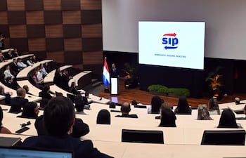 Manuel Ochipintti en traje oscuro, hablando desde un atril, mientras asistentes en trajes formales escuchan atentamente.