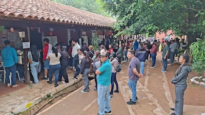 Multitud de personas en fila en un centro de votación, algunas conversando, ambiente de actividad y espera.