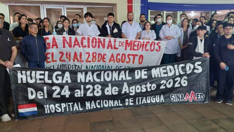 Médicos en batas blancas sosteniendo pancartas sobre la huelga nacional, algunos usando mascarillas en un ambiente hospitalario.