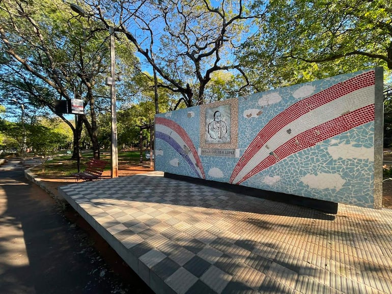 Mural colorido en un parque desierto, con árboles verdes y pavimento visible, en un día soleado.