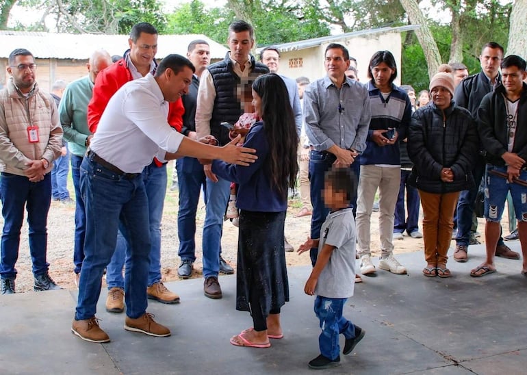 Diego Candia agachado interactúa con una niña vestida de chaqueta oscura y un niño curioso a su lado en ambiente rural.