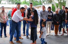 Diego Candia agachado interactúa con una niña vestida de chaqueta oscura y un niño curioso a su lado en ambiente rural.