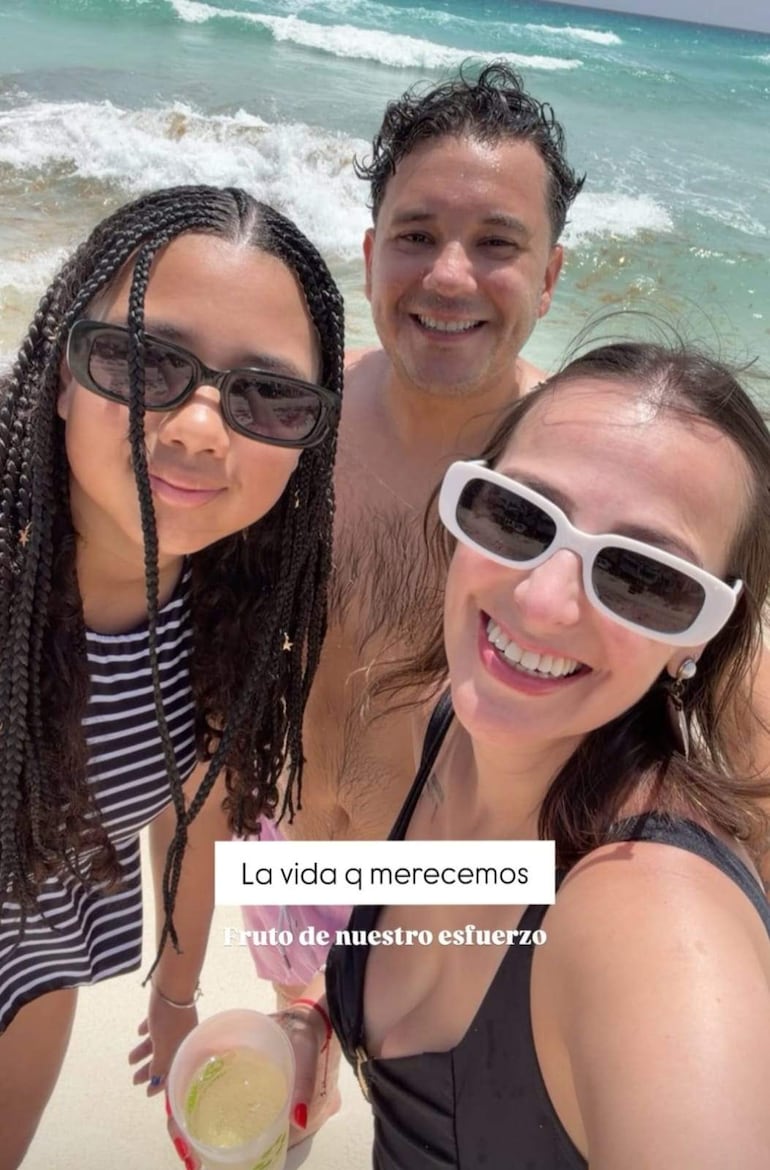 Joven con trenzas y gafas negras, hombre con cabello rizado y torso desnudo, mujer con gafas blancas, todos sonrientes en la playa.