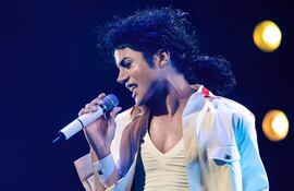 Cantante con cabello rizado y camisa blanca, sosteniendo un micrófono en un escenario iluminado durante su actuación.