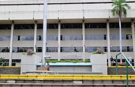 Edificio moderno de la ANDE con fachada de hormigón y banderas, macetas con flores junto a escalinata de peldaños amarillos.