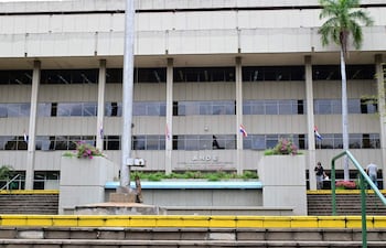 Edificio moderno de la ANDE con fachada de hormigón y banderas, macetas con flores junto a escalinata de peldaños amarillos.
