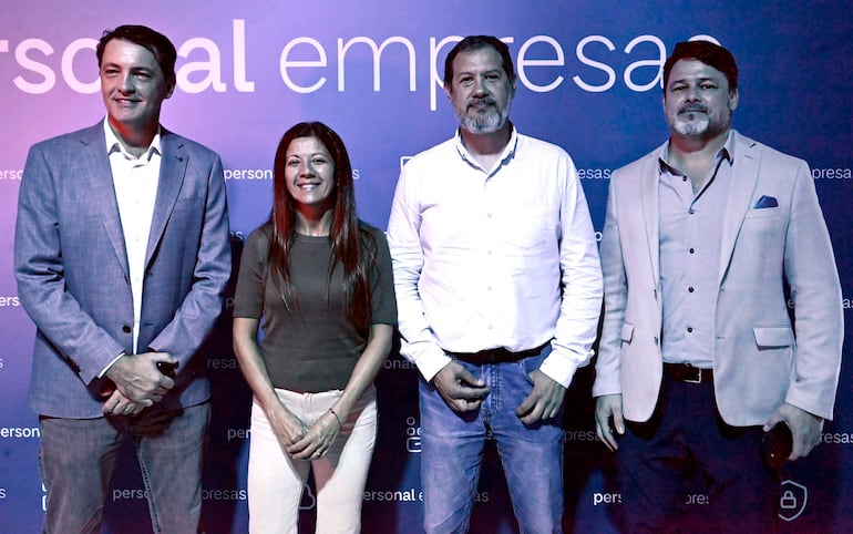 Hombre con saco gris y camisa blanca, mujer con blusa y pantalones claros, hombre canoso con barba, y hombre en chaqueta gris claro, todos sonrientes.