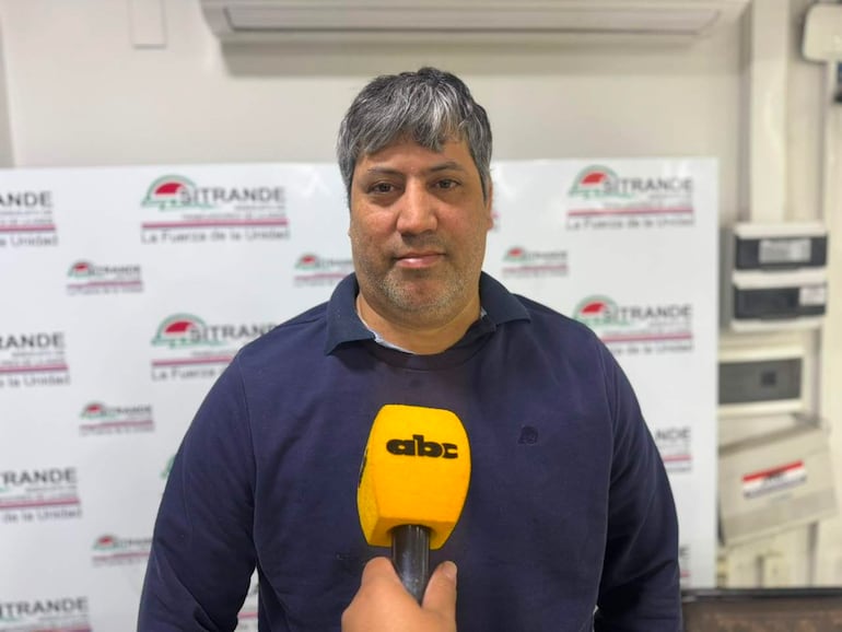 Adolfo Villalba, con cabello canoso y barba, sostiene un micrófono mientras habla frente a un cartel de 'SITRANDE'.