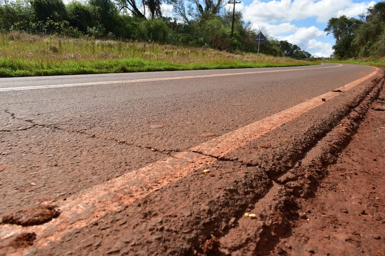 Carretera desierta en mal estado, con asfalto marrón y vegetación a los lados, sin personas visibles.