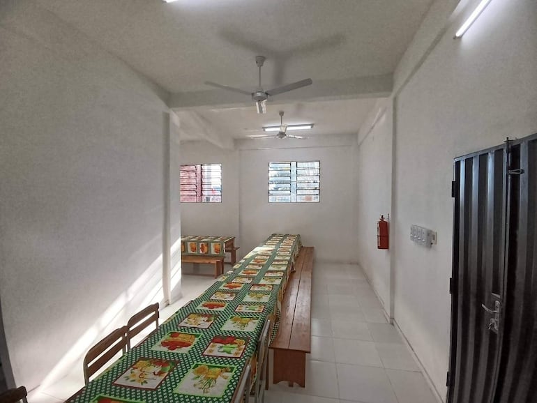 Aula iluminada con mesa de madera y sillas, decorada con mantel colorido, sin personas presentes.