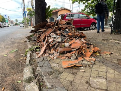 Un montículo de escombros en la acera, mientras una persona camina con abrigo y mochila cerca de vehículos en movimiento.
