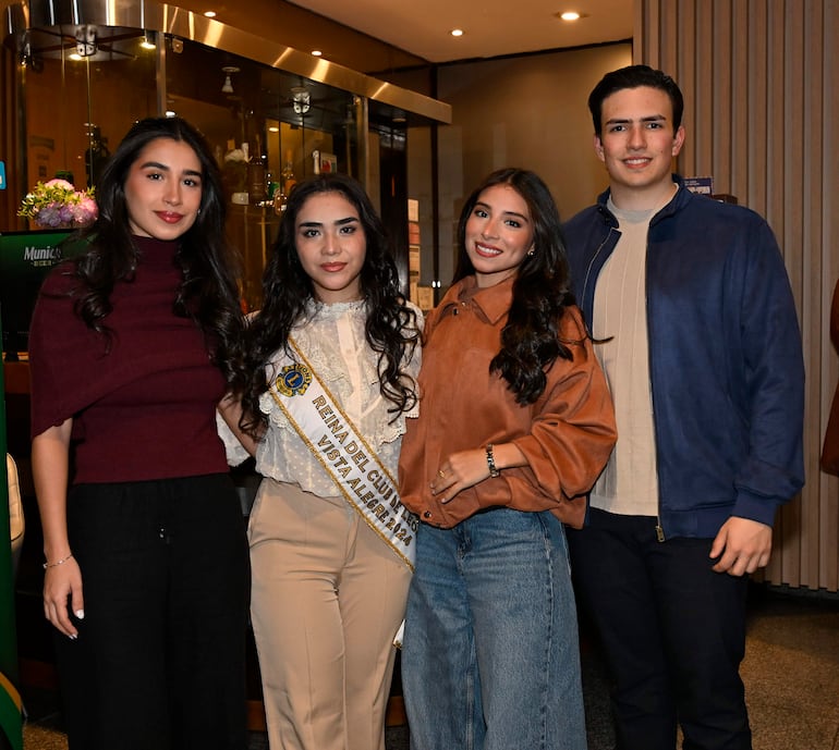Mujer con banda 'Reina del Club' sonriendo en el centro, acompañada de tres personas en un salón elegante.